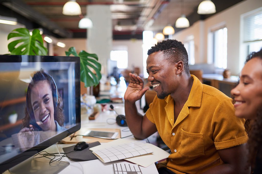 A Black man waves to his colleague on a video call from his office. High quality photo