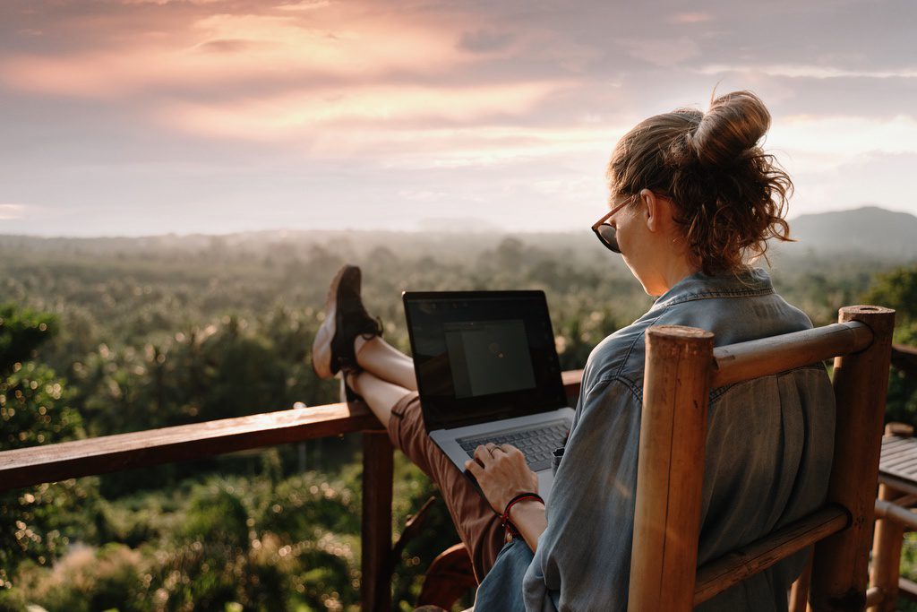 Woman with laptop resting on balcony outdoors while taking break from remote work