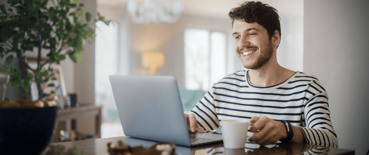 Smiling employee working remotely in home with laptop and cup of coffee