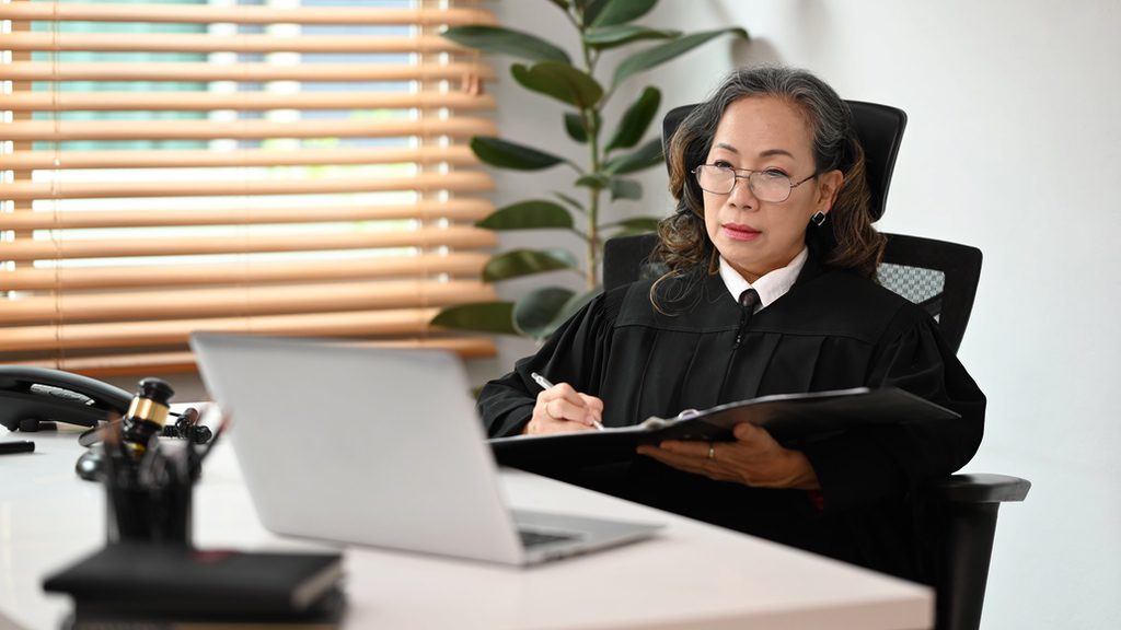 Woman in judges robes writing while looking at laptop to symbolize opportunities for technology to streamline processes.