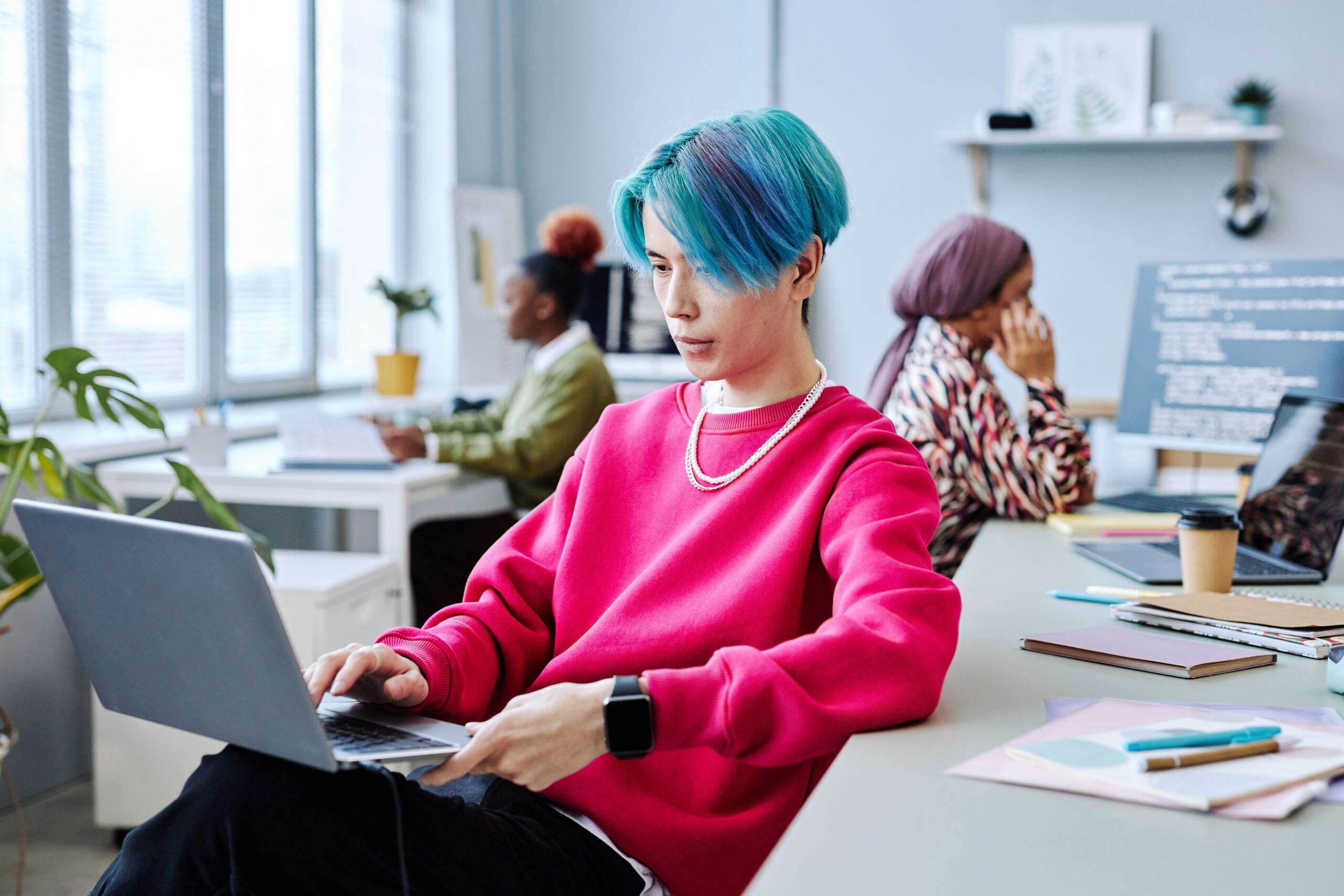 Young man with a laptop on his lap working in a modern art design office looking at people counting technology data and workplace analytics.