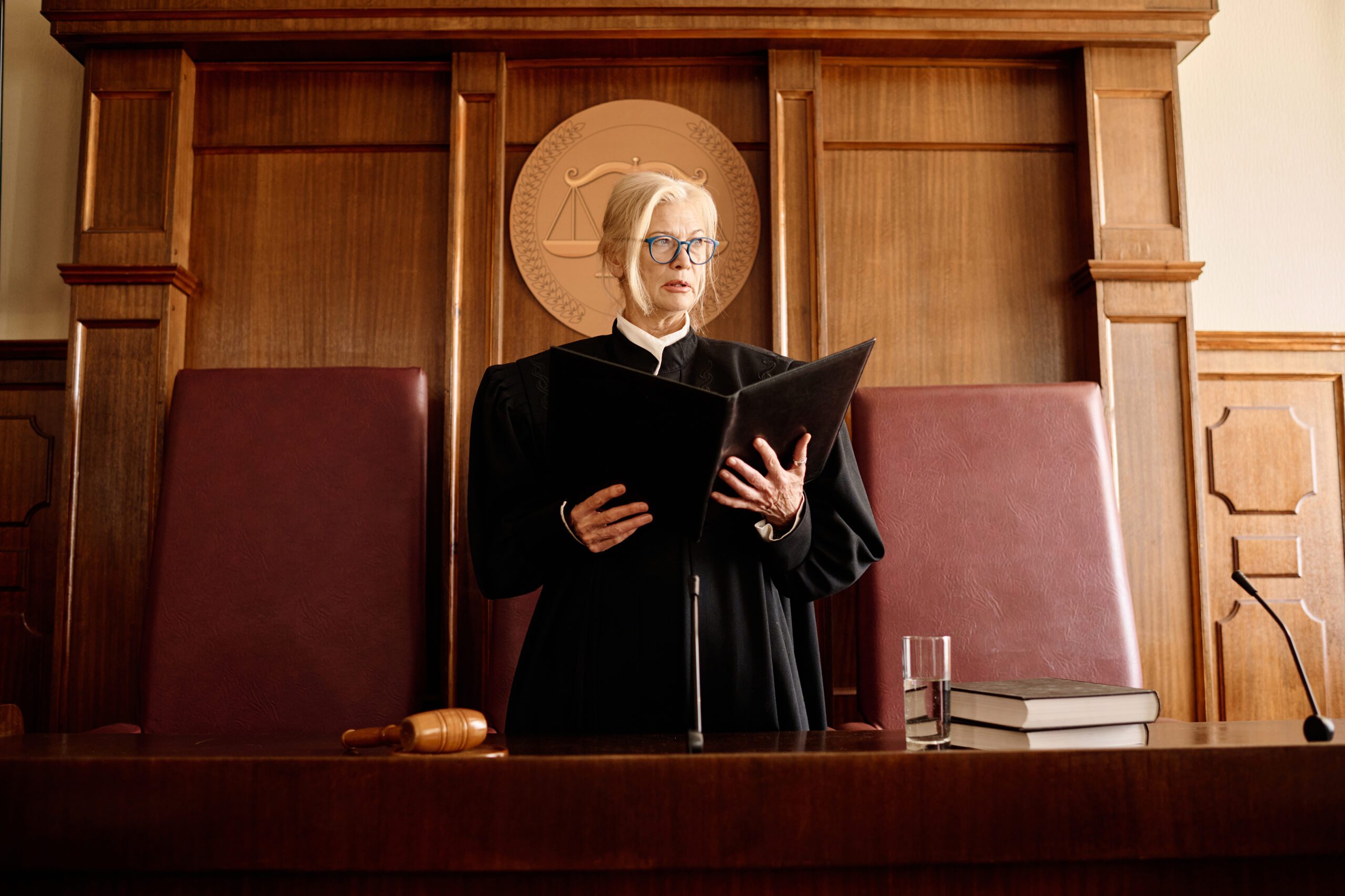 Blonde female judge reading from a folder behind the bench