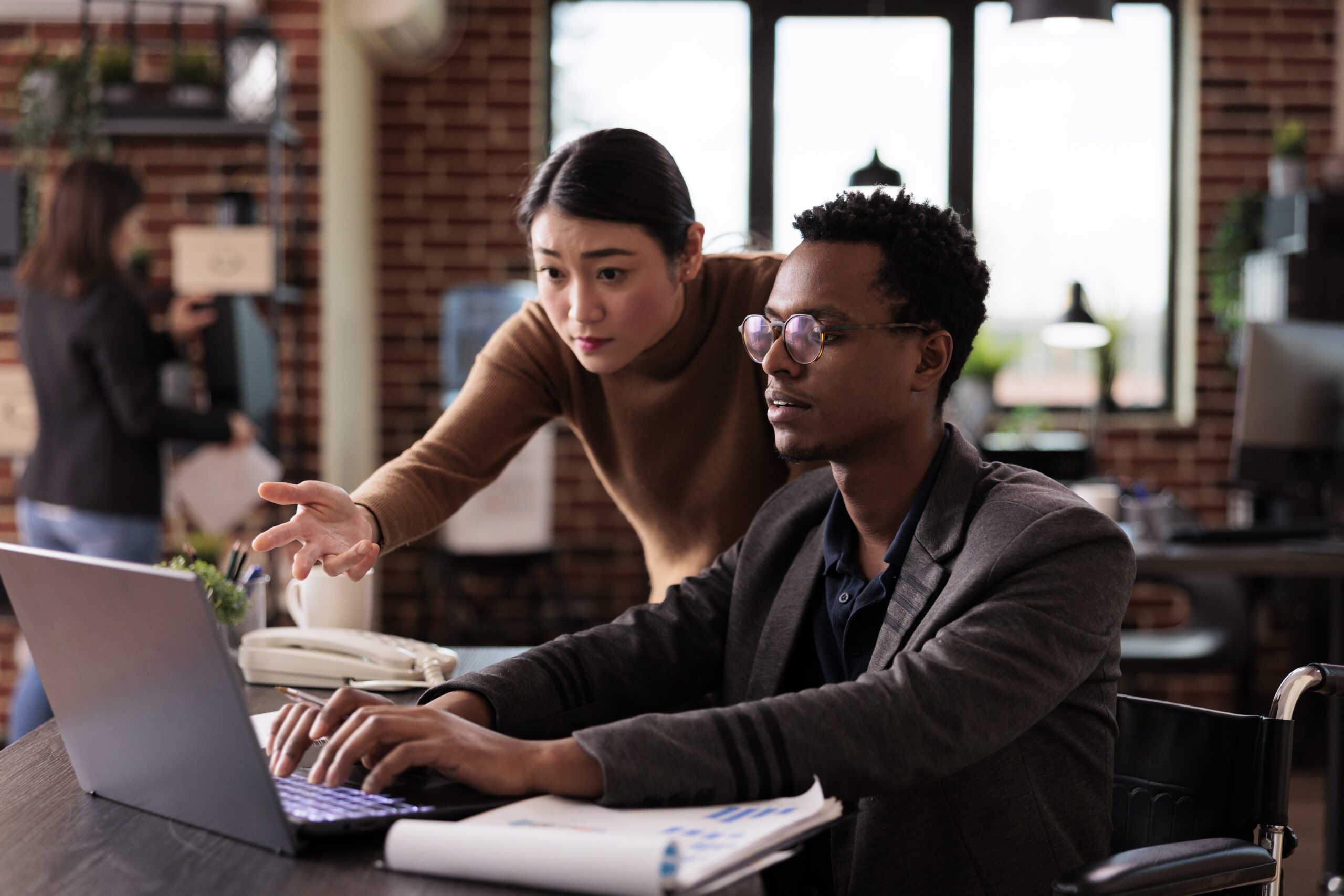 A young man and woman in a modern office analyze people counting technology on a laptop.